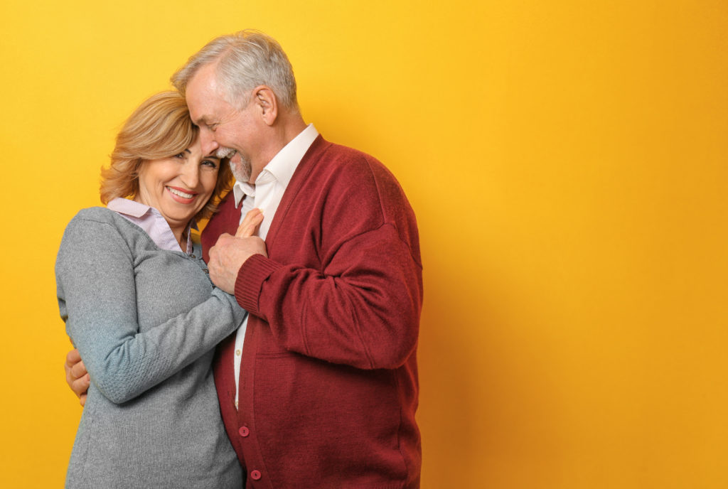 Older man and woman hugging in front of a yellow background