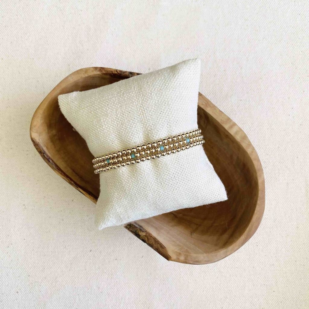 Bracelet stack on a mini pillow on top of a wooden jewelry dish