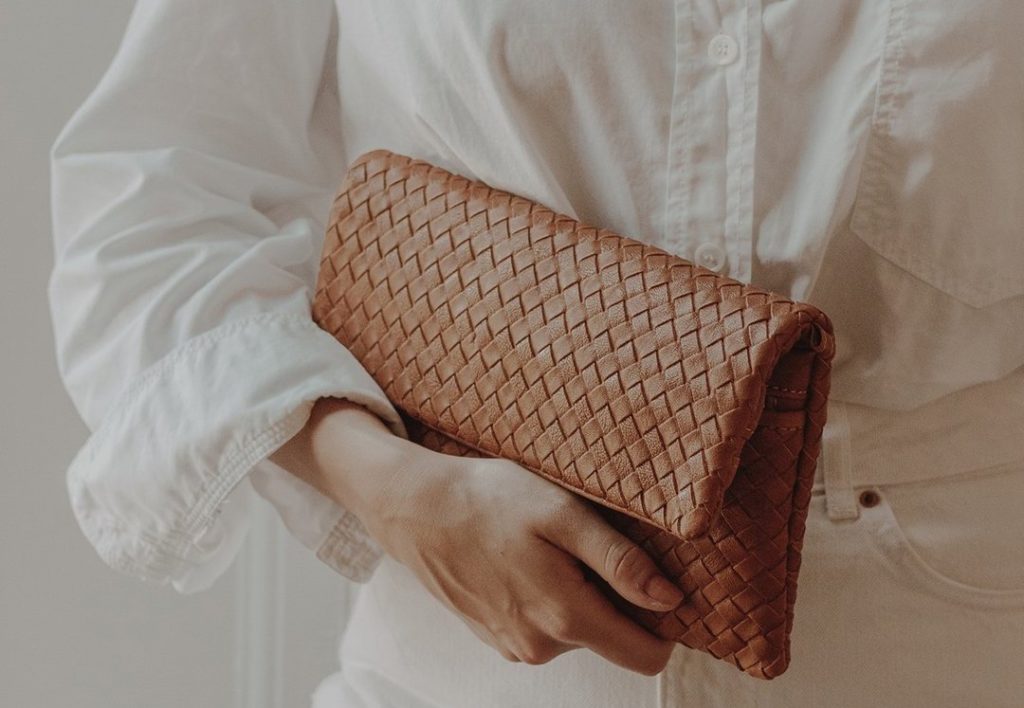 Model holding a woven caramel colored clutch