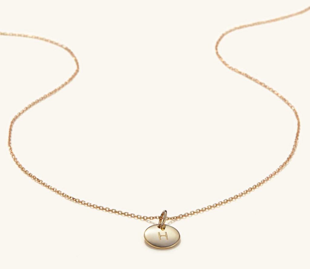 Gold necklace with a circle pendant engraved with the letter H
